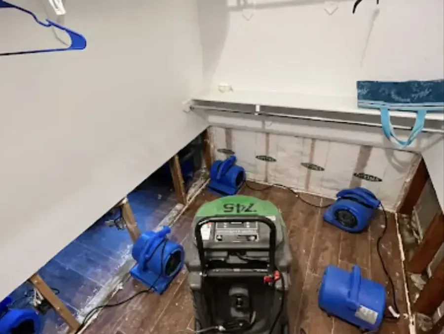 Opened lower walls with air movers and a dehumidifier drying a room