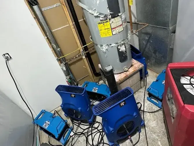 Air movers and drying equipment surround a water heater closet