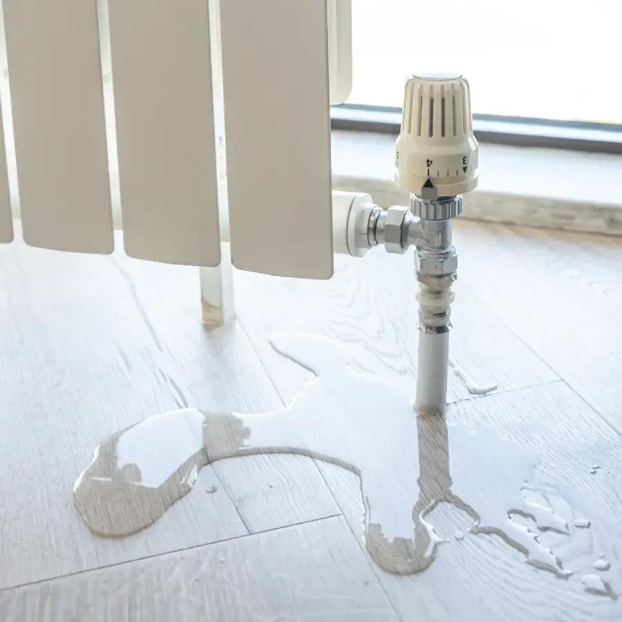 Water pools beneath a radiator valve on pale flooring