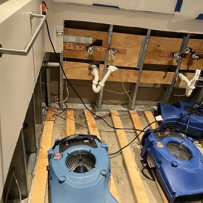 Blue drying fans surround exposed flooring below an opened sink cabinet