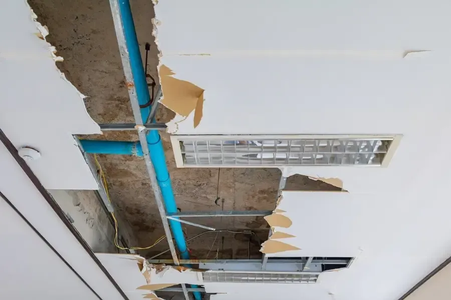 An open ceiling reveals plumbing above water-damaged finishes