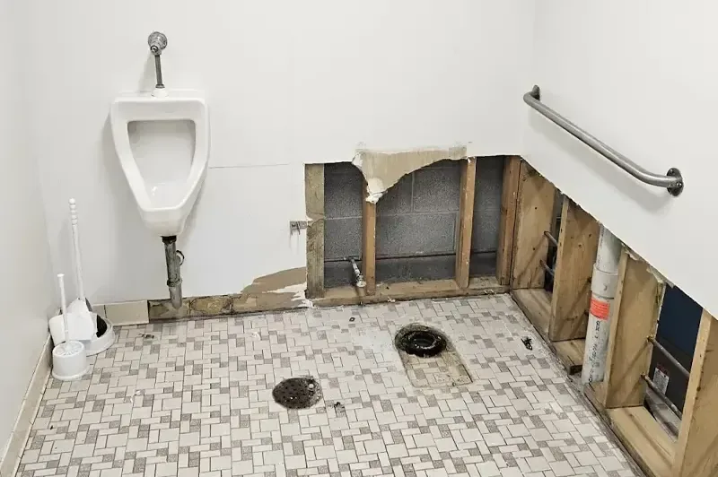 A restroom has exposed lower wall framing beside a floor drain